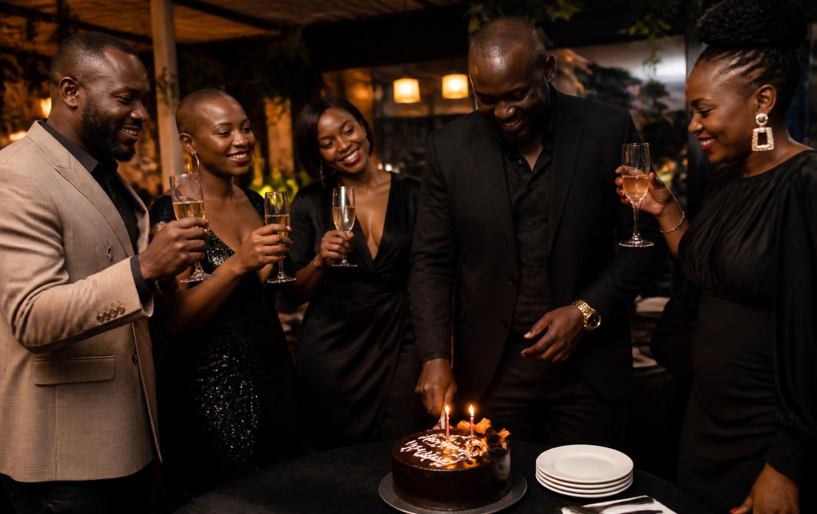 Friends in evening wear raising glasses around a candlelit cake at a milestone birthday in Nairobi