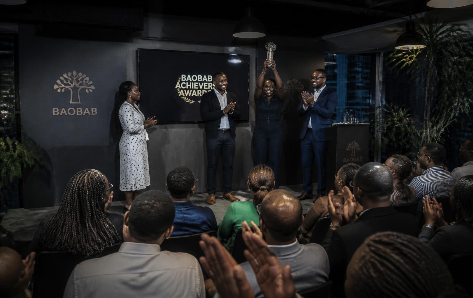 A Kenyan corporate team applauding at a branded stage event in a modern Nairobi office