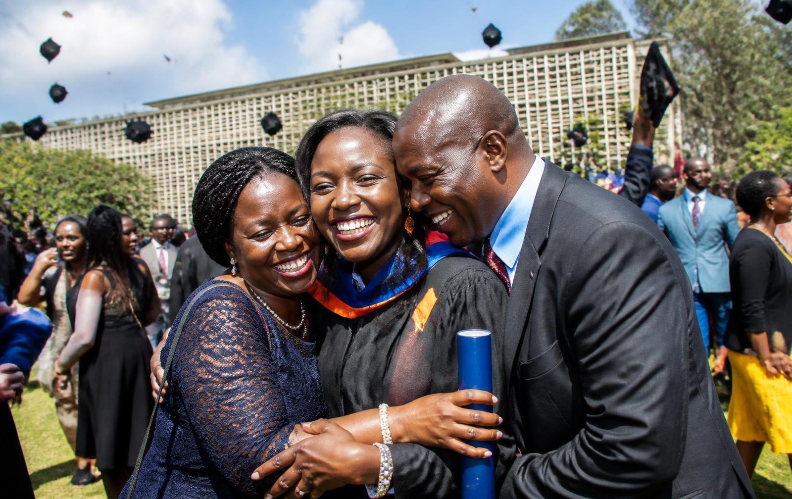 A Kenyan graduate embraced by proud family, mortarboards flying overhead on campus